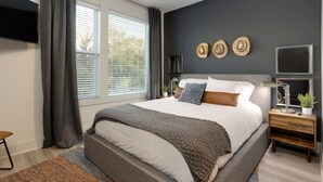 A modern bedroom with a large bed, a bedside table with a lamp, and a TV mounted on the wall.