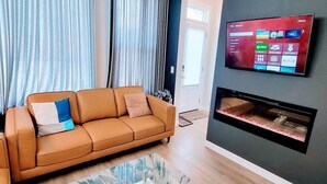 A living room with a sofa, a flat-screen TV mounted on the wall, and a fireplace.
