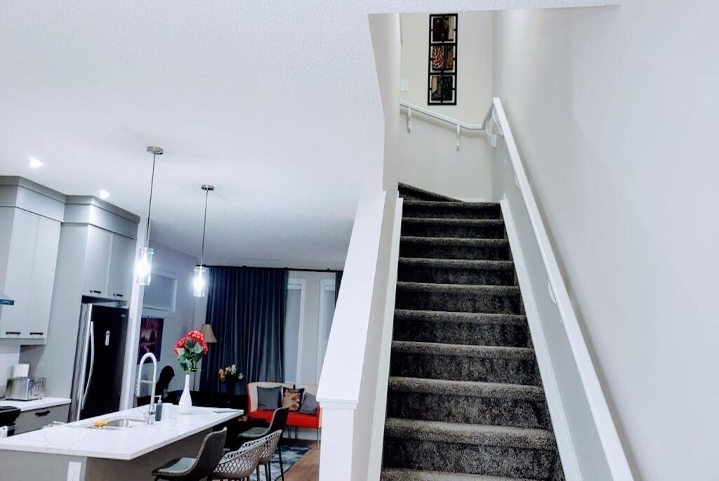 Une cuisine moderne avec un îlot central, un coin repas doté d’un canapé rouge et un escalier avec une rampe noire.