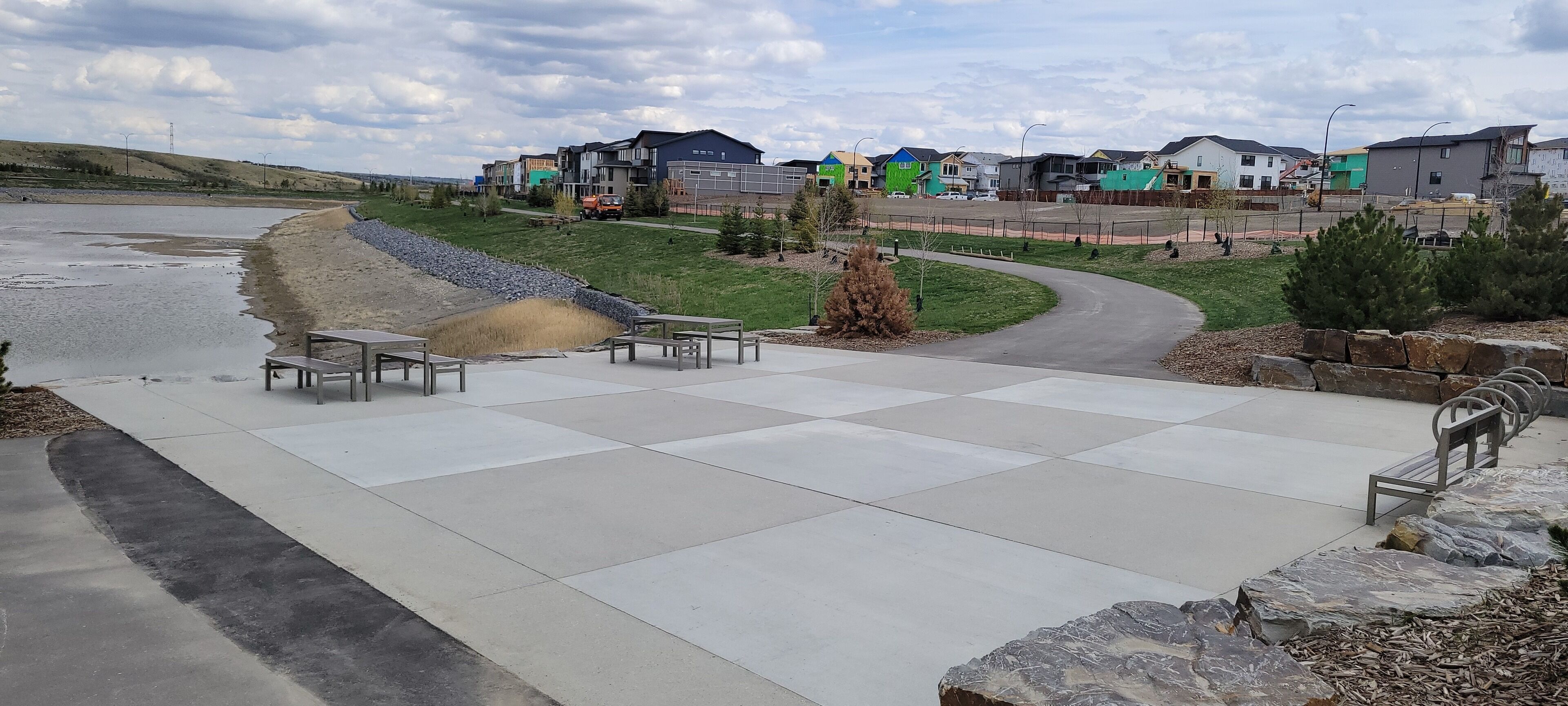 A paved outdoor area with benches and a curved pathway leading to a residential area with colorful houses.