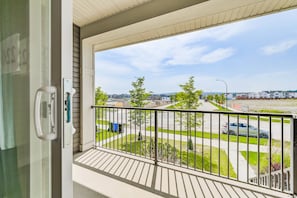 Enjoy the view from this balcony overlooking a quiet residential street with houses, cars, and a lush green area.