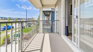 A balcony with a metal railing, a glass door, and a view of a parking lot and buildings in the distance.