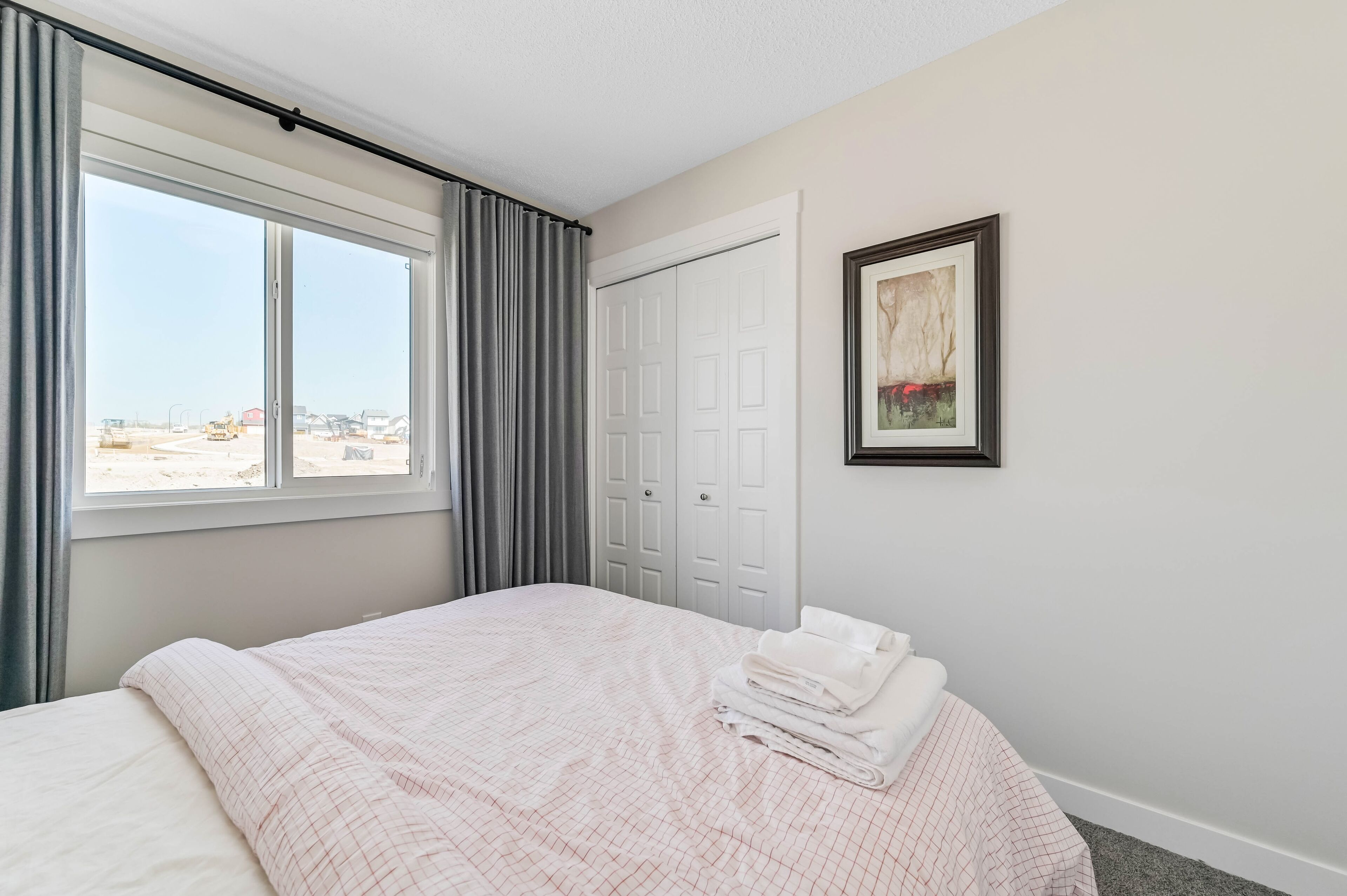 A hotel room with a bed, a window with curtains, a door, and a framed picture on the wall.