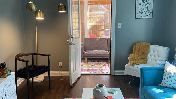 Un salon avec une table basse blanche, un canapé bleu, un tapis à motifs et un lampadaire.