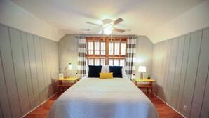 Une chambre à coucher avec un grand lit, un ventilateur de plafond, deux tables de chevet avec des lampes et une fenêtre avec des rideaux.