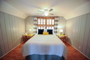 A bedroom with a large bed, two bedside tables, a ceiling fan, and a window with curtains.