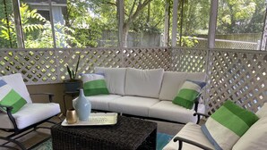 Un patio couvert comprenant un canapé blanc, deux fauteuils, une table basse en osier et une plante en pot.