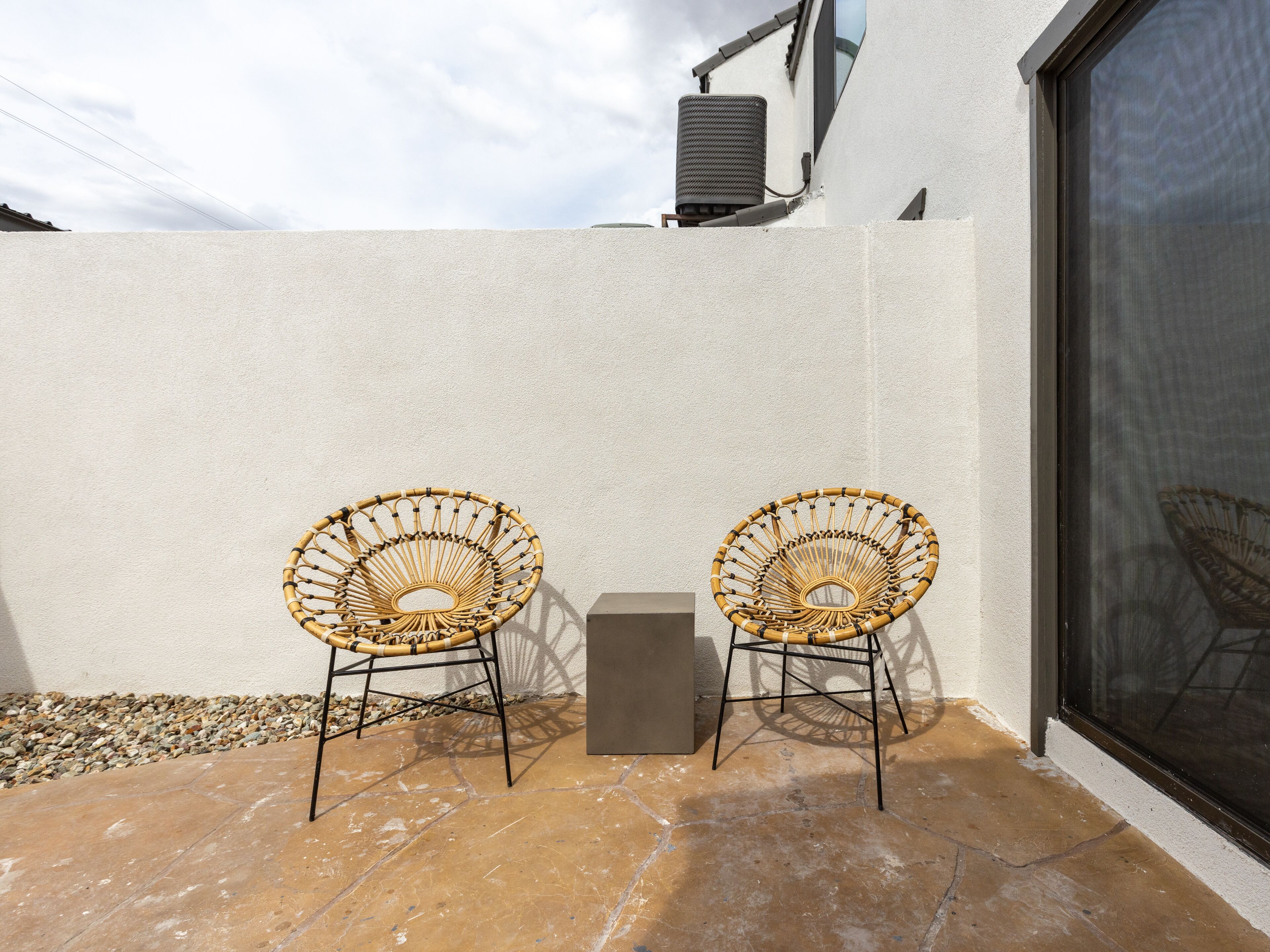 Zwei Korbstühle mit Metallgestellen auf einer gefliesten Terrasse vor einer weißen Wand.