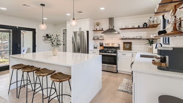 A modern kitchen with a central island, bar stools, stainless steel appliances, and a large window.
