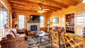 L’intérieur d’une cabane en rondins, avec une cheminée, des meubles en bois et un ventilateur de plafond.