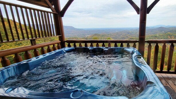 Un bain à remous sur une terrasse en bois, offrant une vue panoramique sur les montagnes et les vallées.