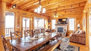 L’intérieur d’un chalet en bois comprend une table à manger, des chaises, un canapé, une cheminée et un téléviseur.