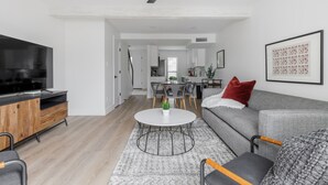 Ein modernes Wohnzimmer mit Flachbildfernseher, grauem Sofa, rundem Couchtisch und Deckenventilator.
