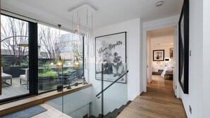 A modern interior with a glass staircase, a framed poster, and a view of an outdoor patio. - Luxe 3b/3b duplex w/ terrace, BBQ & parking. Near Kings Cross & central London. (London)