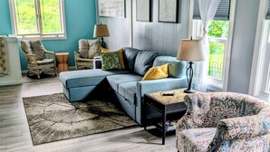 A living room with a sofa, armchairs, a patterned armchair, a coffee table, a rug, and a window with curtains. - Cottage On The Canal - An All Seasons Getaway - Waterford - Lake Tichigan (Waterford)