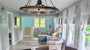 A dining area with a wooden table and benches, a living room with a blue sofa and patterned cushions, and a chandelier with exposed bulbs. - Cottage On The Canal - An All Seasons Getaway - Waterford - Lake Tichigan (Waterford)