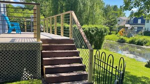 A wooden staircase leading to a deck with a metal railing, surrounded by a grassy area and a small pond. - Cottage On The Canal - An All Seasons Getaway - Waterford - Lake Tichigan (Waterford)