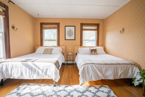 A room with two beds, a patterned rug, and a framed artwork on the wall.