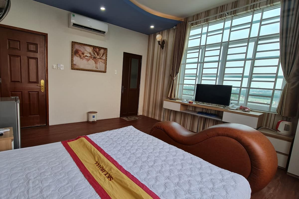 Une chambre d’hôtel avec un lit, un bureau avec un ordinateur, une télévision et une fenêtre avec des rideaux.