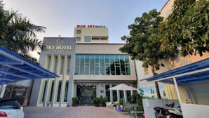 A hotel with a prominent sign reading "SKY HOTEL" and "BLUE SKY HOTEL" above it. There are covered parking areas and a few vehicles parked in front. - Sky Hotel by Zuzu (Tam Hiep)