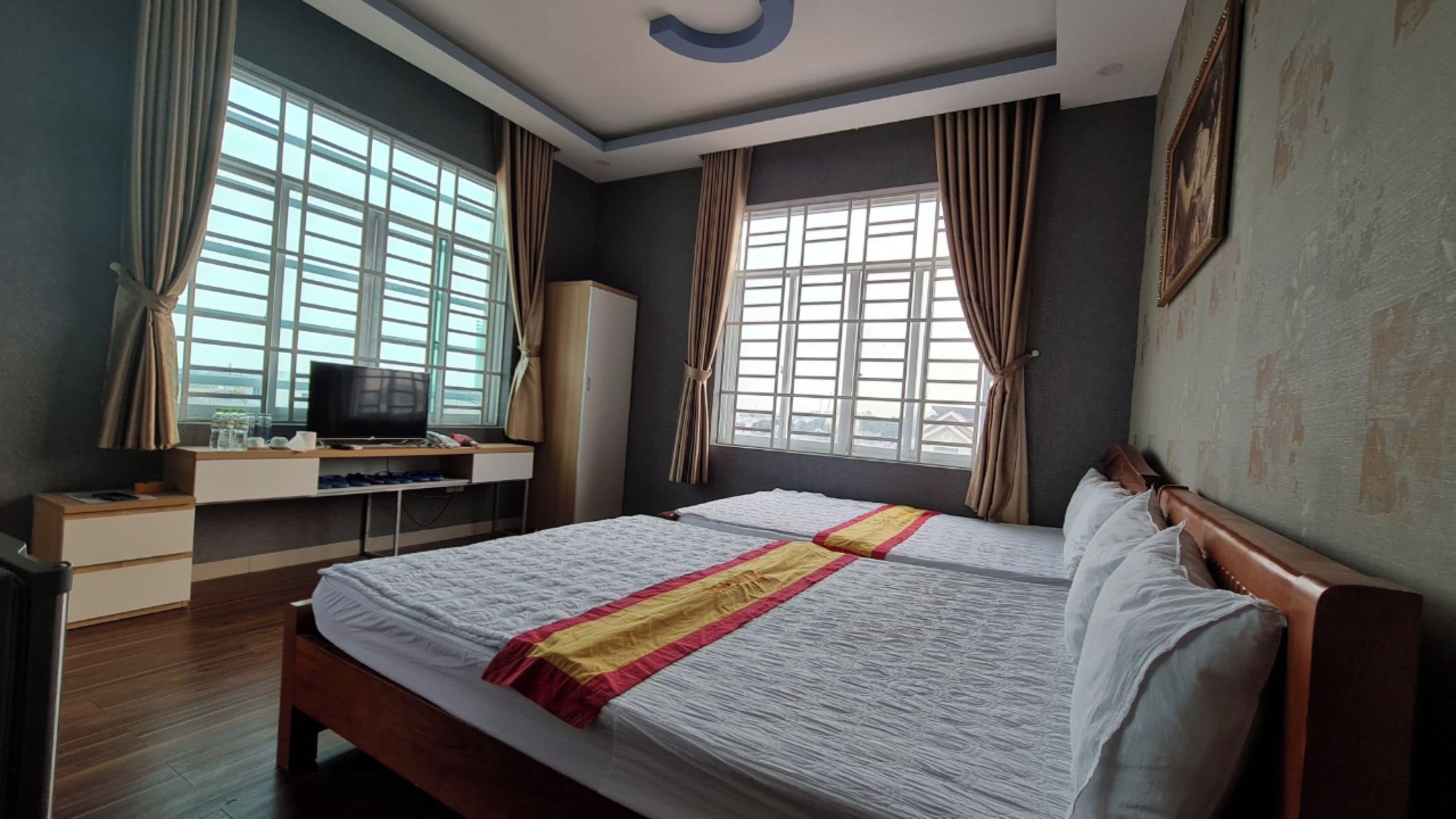 A hotel room with a large bed, a desk with a television, and windows with curtains.