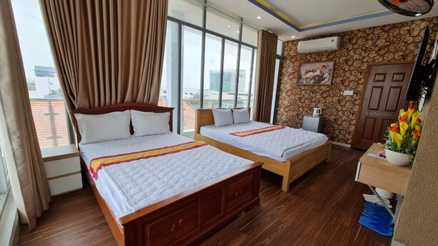 A hotel room with two wooden beds, large windows, a view of the city, and a decorative wall. - Sky Hotel by Zuzu (Tam Hiep)