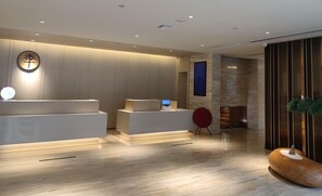 A modern reception area with a wooden reception desk, a digital screen, and a red chair. - Ji Hotel (Hefei)