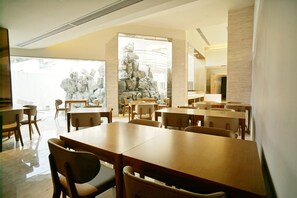A modern dining area with wooden tables and chairs, a large window with a view of rocks, and a stone wall feature. - Ji Hotel (Hefei)