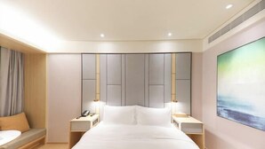 A hotel room with a large bed, bedside tables, a sofa, and a painting on the wall.