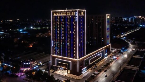 A high-rise building with multiple floors, illuminated by internal lighting, surrounded by a cityscape at night.