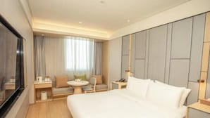 A hotel room with a large bed, a TV, a sofa, a small table, and a nightstand.