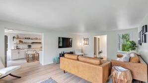 A modern living room with a sofa, a coffee table, and a TV. There is a kitchen area with a countertop and cabinets. - Walk to Shops & Dining – Renovated Gem (Sister Bay)