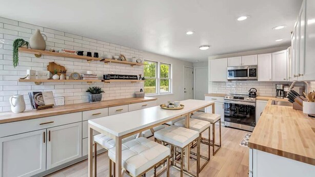A modern kitchen with white cabinetry, a central island with seating, and built-in appliances. - Walk to Shops & Dining – Renovated Gem (Sister Bay)