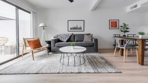 Un salon moderne avec un canapé gris, une table basse ronde et un coin repas comprenant une table et des chaises en bois.