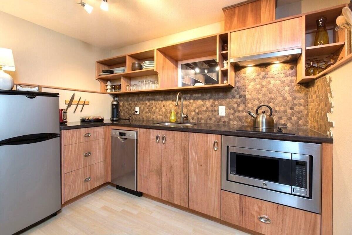 Eine moderne Küche mit Holzausbau, einem Edelstahlkühlschrank, einem Geschirrspüler, einer Mikrowelle und einer gefliesten Spritzschutzwand.