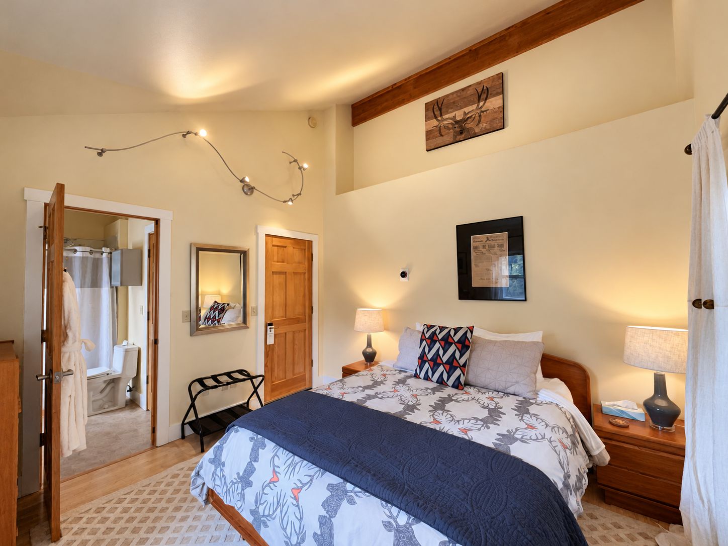 A bedroom with a bed, bedside lamps, a wooden door, a mirror, and a wall-mounted picture.