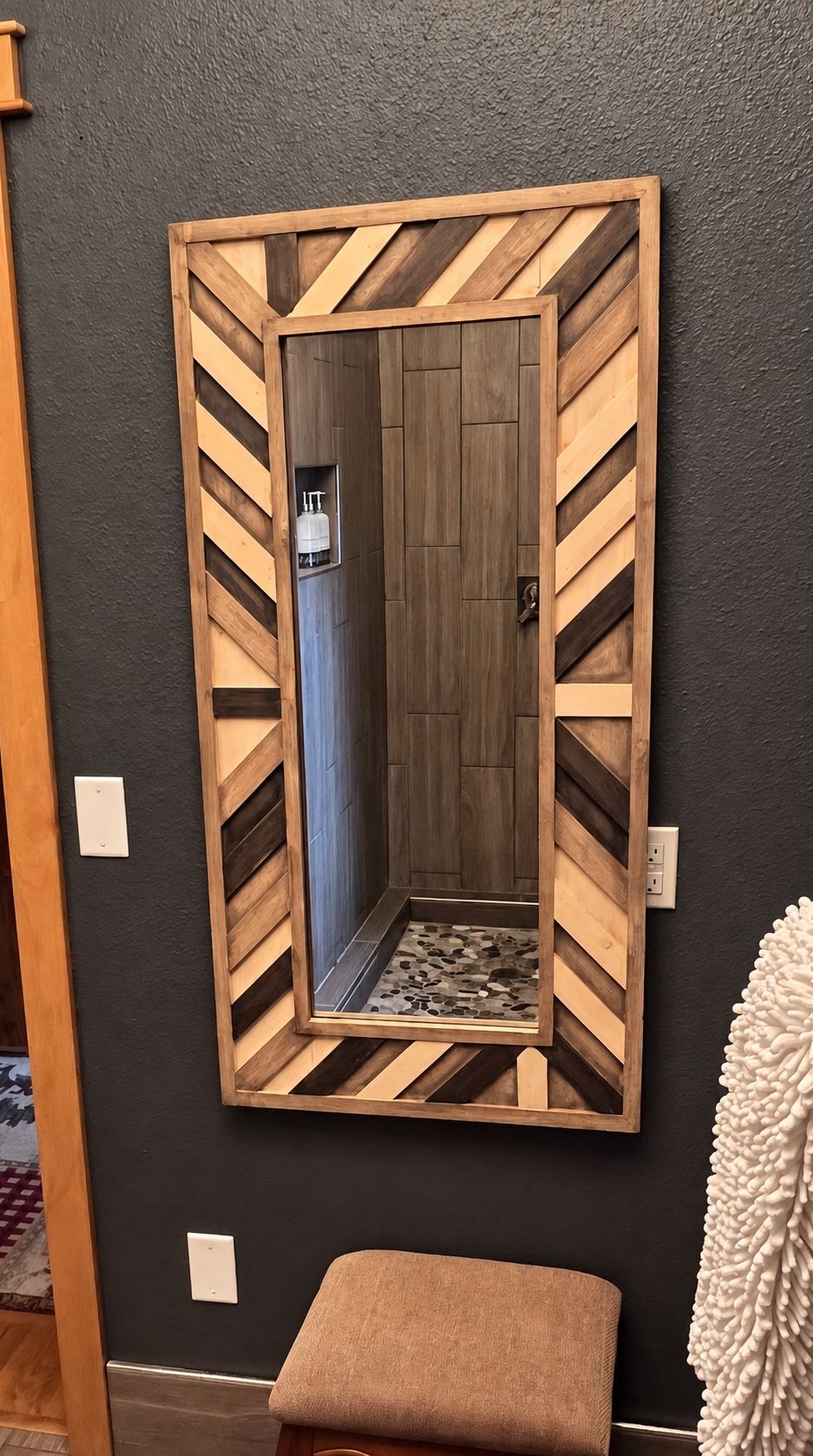 A mirror with a wooden frame and a geometric pattern, mounted on a dark wall.