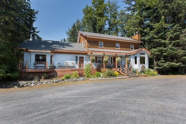 A two-story log cabin with a porch and a star decoration on the front door. - Bell In The Woods B&B (Seward)