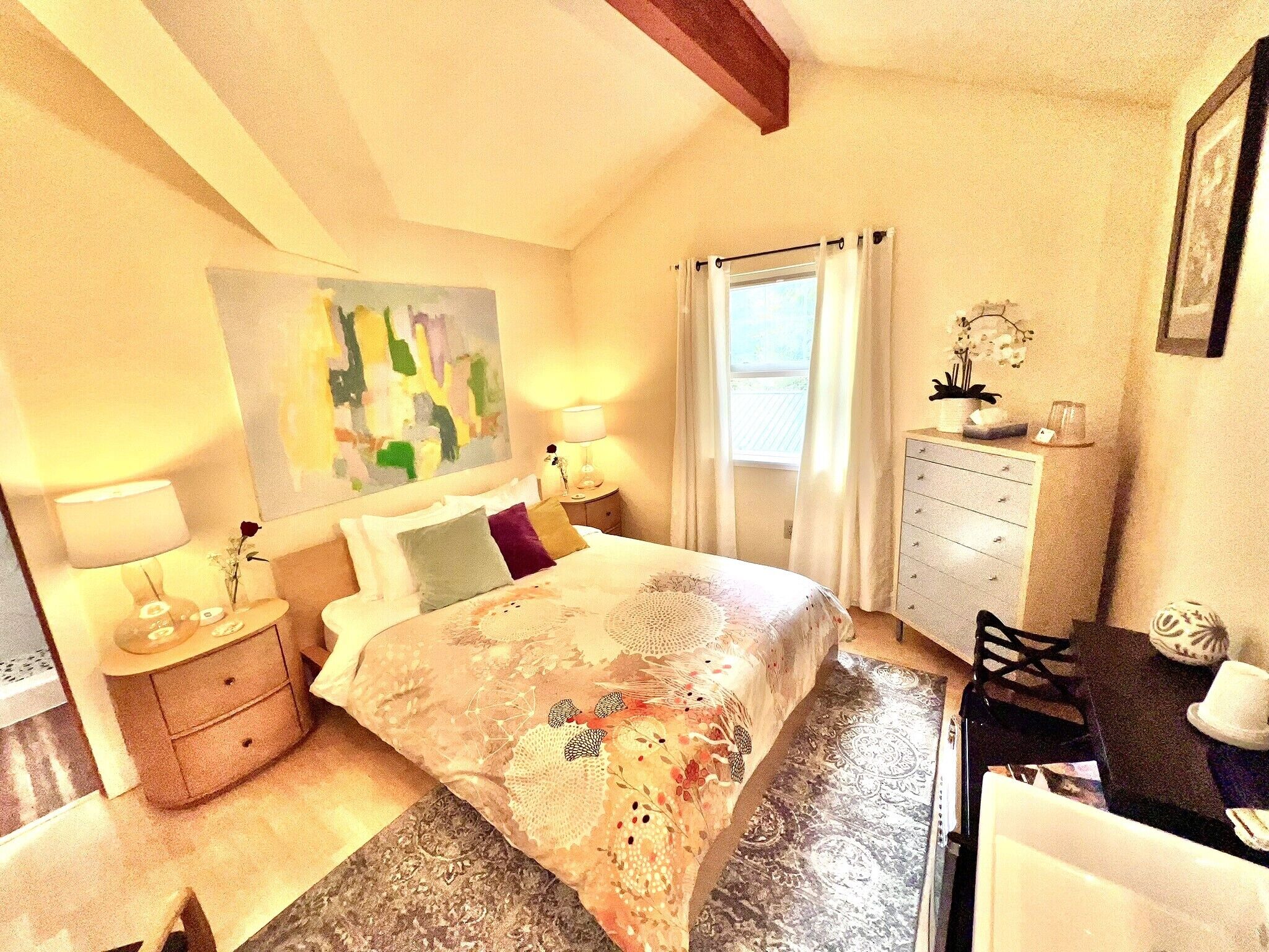 A bedroom with a bed, bedside tables, a dresser, a desk, and a window with curtains.