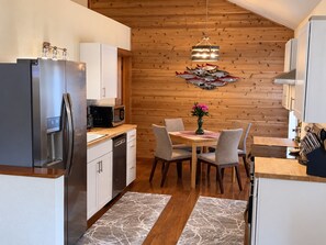 Cocina compacta con electrodomésticos modernos, zona de comedor con mesa y sillas, y pared de madera decorada con un pez.