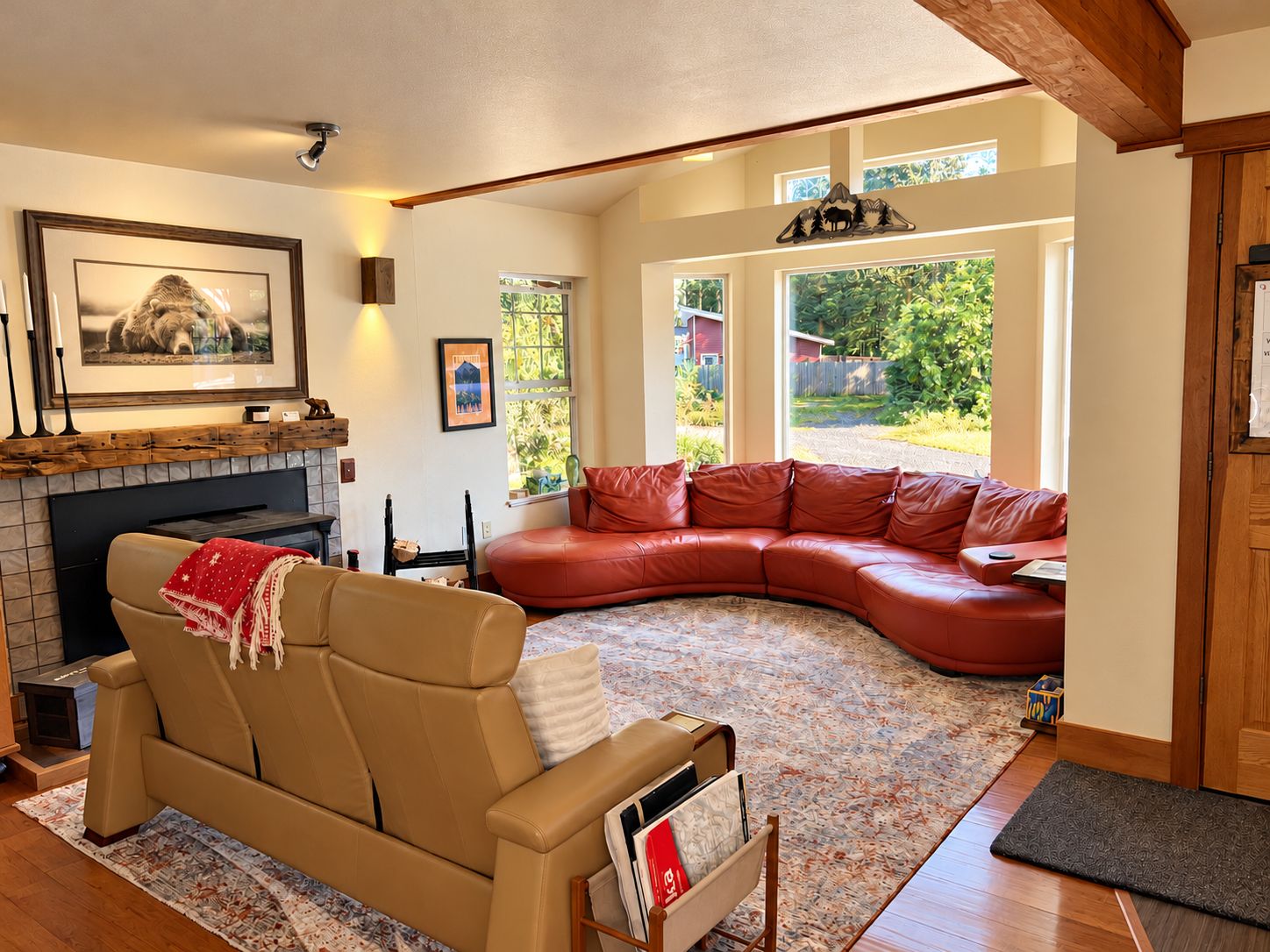A living room with a fireplace, a large window, a red leather sofa, and a tan leather couch.