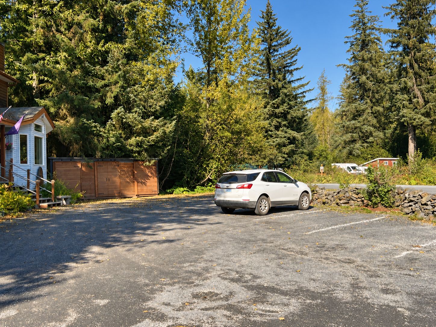 A white SUV parked in a driveway with a wooden shed and a small house in the background.
