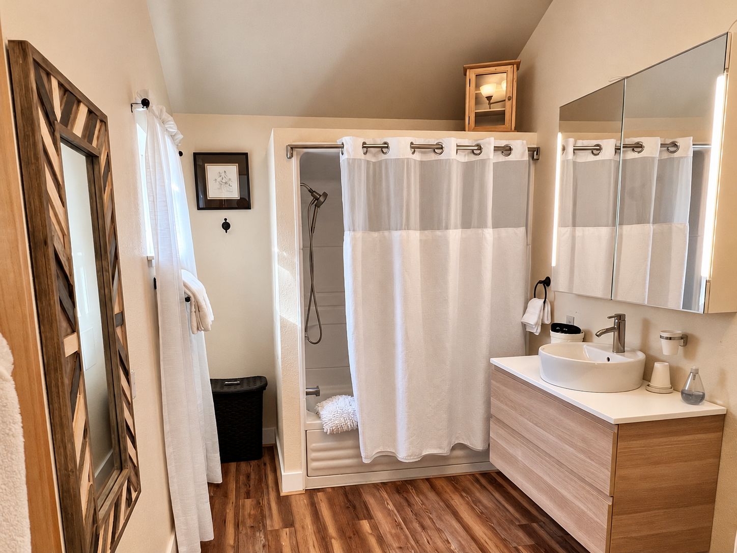 A bathroom with a shower, a sink, a mirror, and a framed picture on the wall.