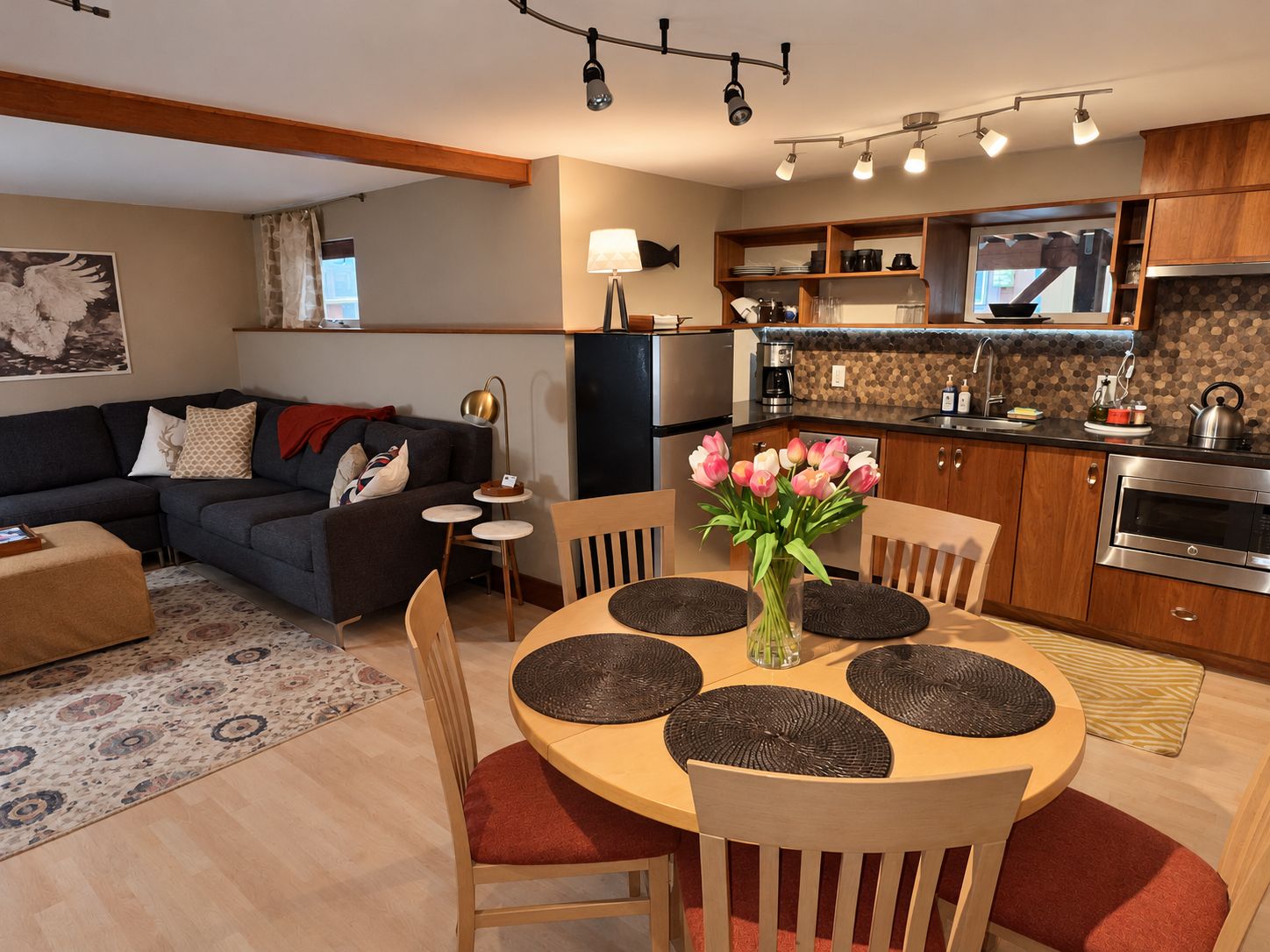 A modern kitchen with a built-in oven, a dining area with a round table and chairs, and a living room with a sofa and a coffee table.
