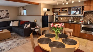 A modern kitchen with a built-in oven, a dining area with a round table and chairs, and a living room with a sofa and a coffee table.