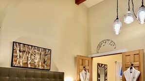 Quarto de hotel com uma cama grande, cabeceira de madeira, uma obra de arte emoldurada acima da cama e dois roués pendurados em uma porta.