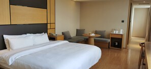 Une chambre d’hôtel avec un grand lit, un bureau, une chaise et une petite table sur laquelle se trouvent une tasse et une bouteille.