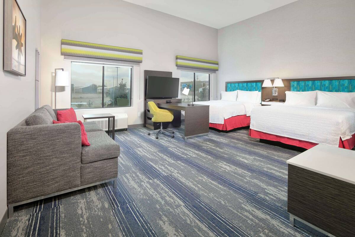 A hotel room with a sofa, a desk, a TV, two beds, and a view of the outside.