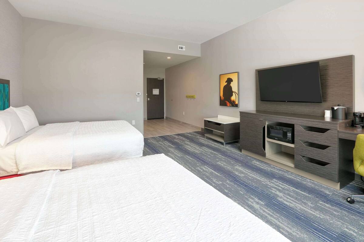 A modern hotel room with a large bed, a TV mounted on the wall, a desk with a microwave, and a small seating area.