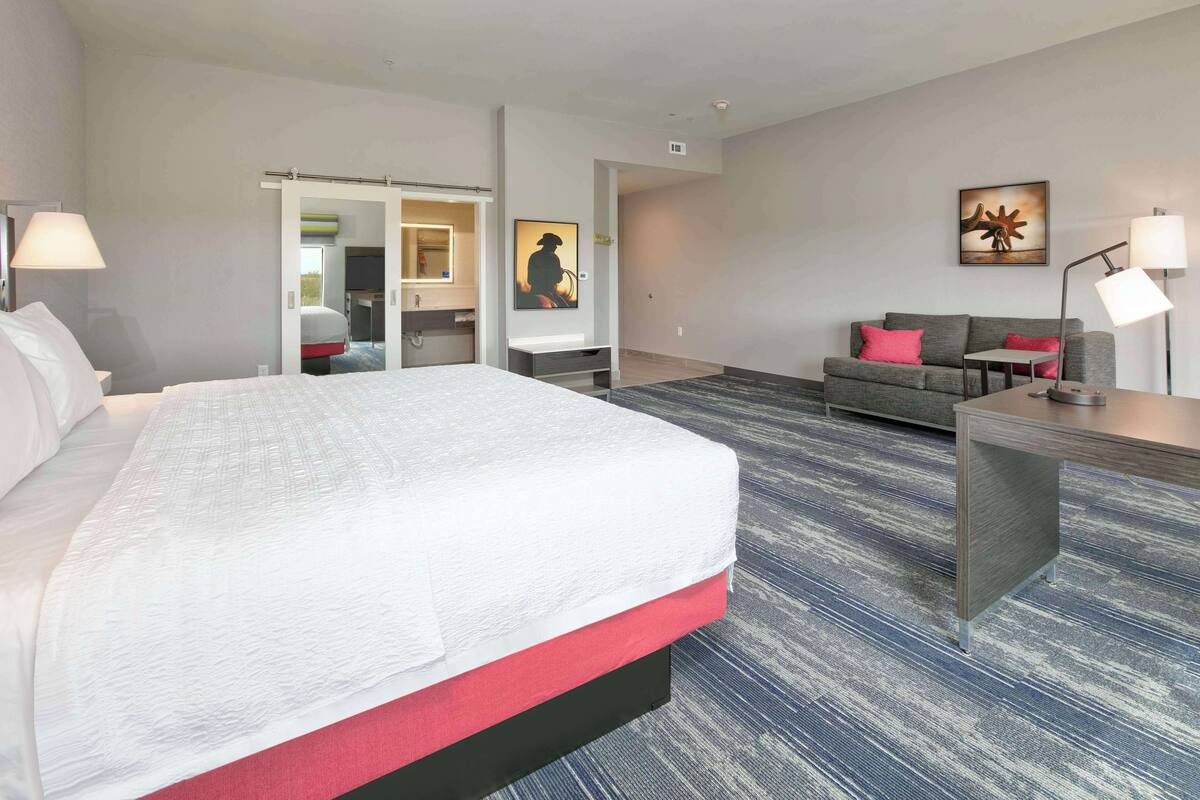 A hotel room with a large bed, a sofa, a desk, and a mirror.